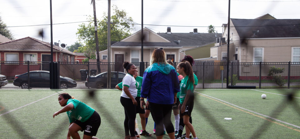 Girls Coach Katie Lucky-Heard (left, white shirt) delivered a half-time pep talk to her team. “Tú puedes,” she said. You can do it.
